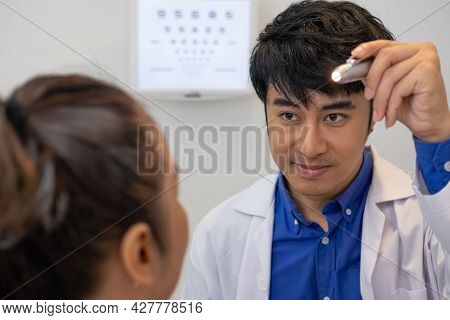 Selective Focus At Optometrist Face. While Doctor Using Penlight And Subjective Refraction To  Exami