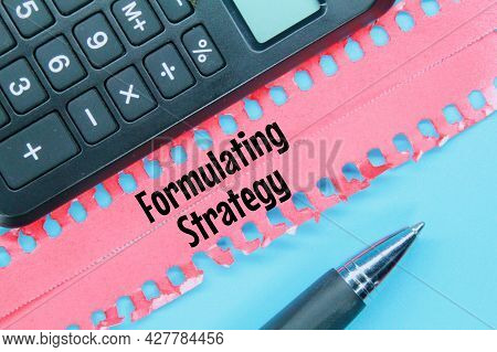 Calculator, Torn Paper, Pen With The Word Formulating Strategy