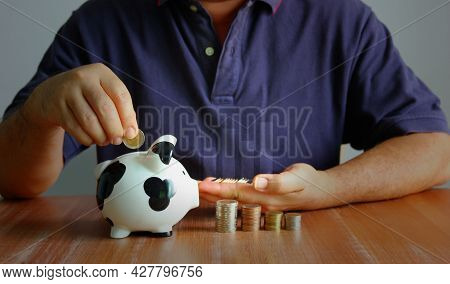 Asian Man Putting Coin In To Piggy Back With Coin Stacking And Trend Graph. Man Is Sloving Financial