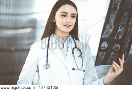 Professional Young Woman-doctor Is Looking At Her Patients Roentgenogram. Physician At Work In A Cli