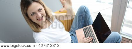 Young Woman With Laptop Sitting In Armchair And Waving Hand