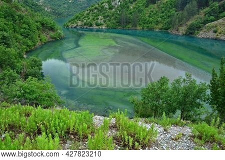 Koman Lake With Colorful Green And Turquoise Water Surrounded By Lush Vagetation
