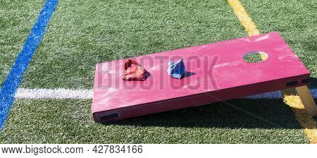A Red Homemade Cornhole Bean Bag Toss Game On A Green Turf Field With Red And Blue Bags On Top.
