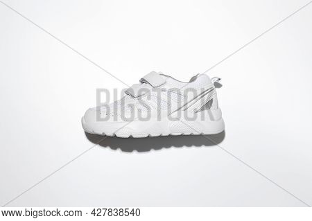 Flat Lay One White Kid Running Shoes With Velcro Fasteners On The Side With Hard Shadows In The Cent