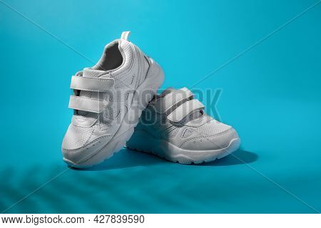 A Balance Of Two White All-purpose Sneakers With Velcro Fasteners On A Blue Background With Fern Sha
