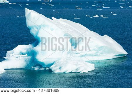 Small Meling Iceberg Calved From Glacier Into The Sea Flpating On Azure Blue Surface Of Ocean Water