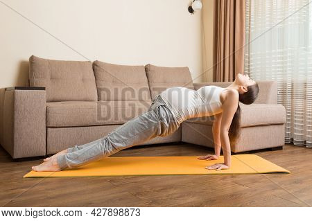 Beautiful Young Pregnant Woman Sitting Near Sofa In Yoga Pose At The Home. Pregnancy Yoga And Fitnes