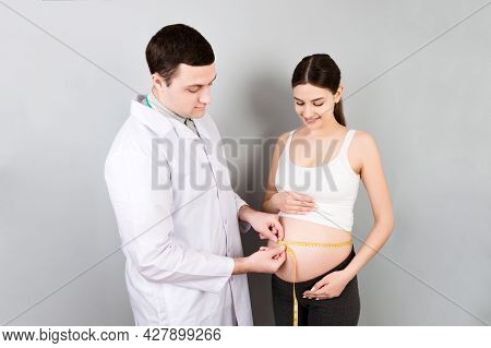 Happy Beautiful Pregnant Young Woman Touching Her Bare Tummy While A Doctor Is Measuring It