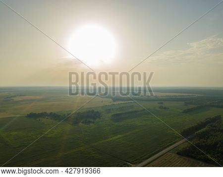 Drone View Of The Sky With The Sun, Fields, Forests, Paved Road At Sunset