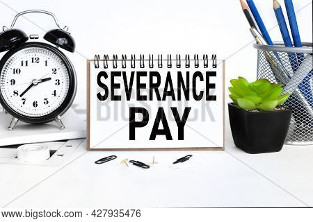 Severance Pay, A Notebook On A Work Table, Near A Desk Clock, A Flowerpot And A Glass With Pencils