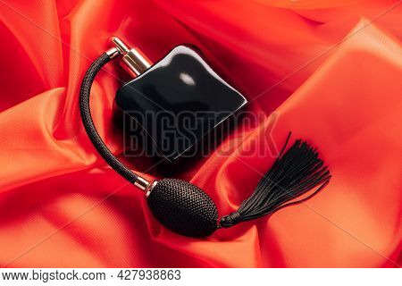 Black Bottle Of Eau De Toilette Or Perfume With Long Tassel Spray Pomp Lies On Red Background Of Flo
