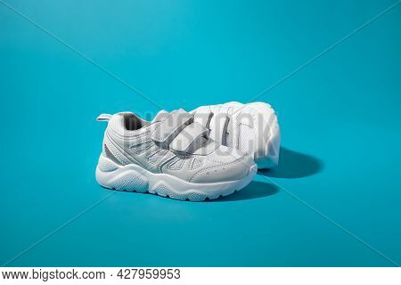 One White Childrens Running Shoe With Velcro Stands In Front Of The Other Lying On Its Side On A Blu