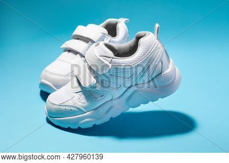 Side View Two Simulated Walking White Woman Sneakers With Velcro Fasteners Isolated On A Blue Backgr