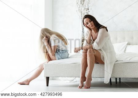 Family conflict and relations concept. Mother and daughter having quarrel and aguring at home. Sad woman and teenage girl sitting on bed. Not looking at each other