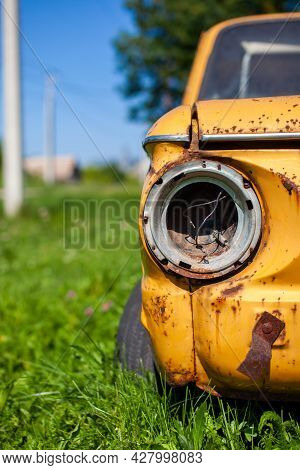 Old Yellow Wrecked Car In Vintage Style. Abandoned Rusty Yellow Car. Closeup Of The Headlights Of Th