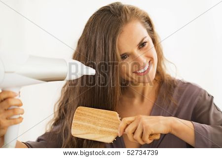 Happy Young Woman Brushing And Blow Drying Hair In Bathroom