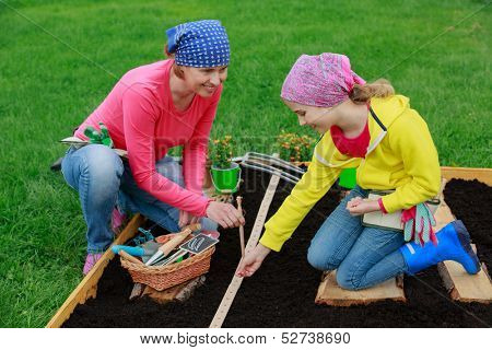 Gardening, sowing seeds to the soil -  girl helping mother in the garden