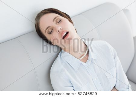 Tired well dressed young woman sitting and sleeping on sofa at home