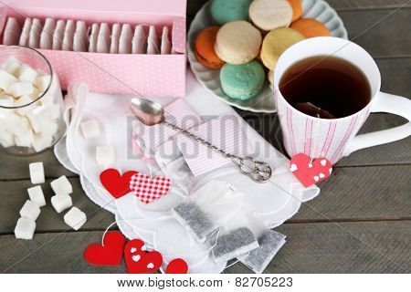 Heart shaped teabag tags, macaroons and cup of tea on wooden background