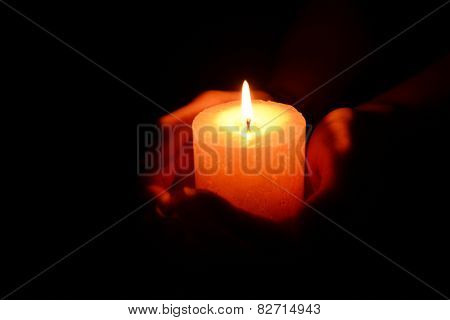 Candle in female hands on black background