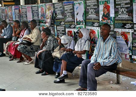 Black People Sit On Bench On Background Of Posters.