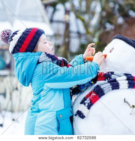 Funny Kid Boy In Colorful Clothes Making A Snowman, Outdoors