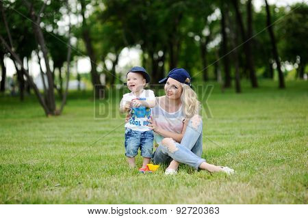 Mom And Baby Son In The Cap On A Background Of Green Grass