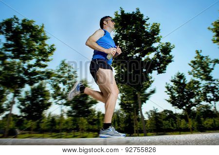 Young Man With Athletic Runner Legs Holding Isotonic Energy Drink While Running In City Park