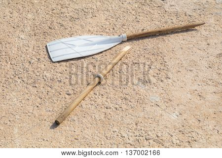 Wooden broken oar, on tan concrete, in the sun.
