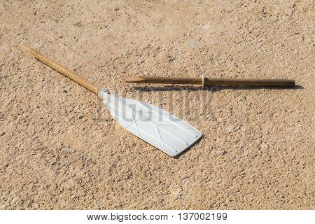 Wooden broken oar, on tan concrete, in the sun.