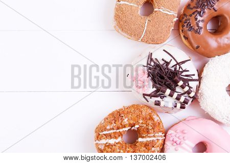 Colored delicious donuts with chocolate coconut and crispy sprinkles on a wooden background. Top view with copy space