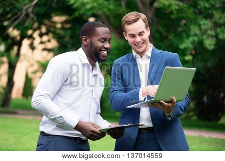 Do it with pleasure. Pleasant cheerful content colleagues using laptop and discussing project while standing outside