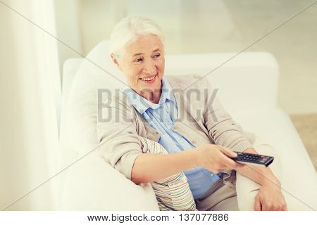 technology, television, age and people concept - happy senior woman watching tv and changing channel with remote control at home