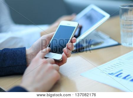 Smartphone touchpad handheld in closeup colleagues working in background.