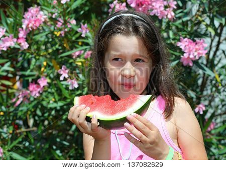 Little Girl With Brown Hair Eating A Slice Of Watermelon In Summ
