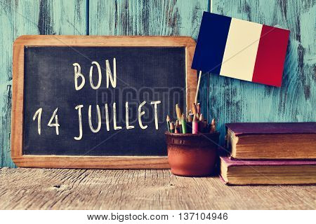 a wooden-framed chalkboard with the text bon 14 juillet, happy 14th of July, the National Day of France, written in French and a flag of France, against a rustic blue wooden background