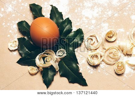 Brown egg on green laurel leaf and excelsior on pack paper background decorated with white flour closeup
