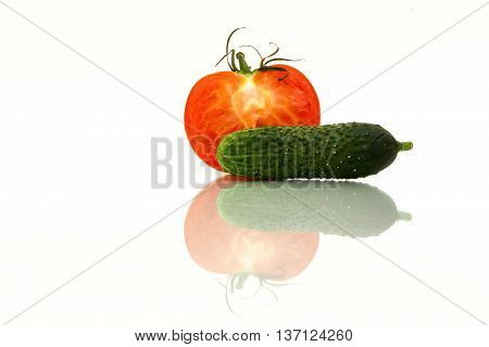 Half of red tomatoes and fresh green cucumber with reflection on white background