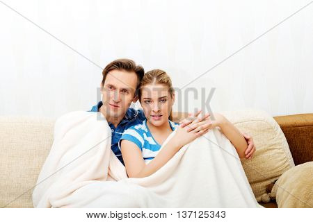 Smiling loving couple sitting on couch with blanket