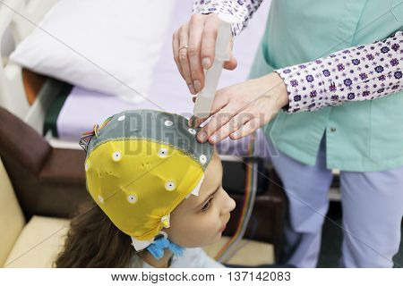 Girl before procedure electroencephalography, nurse using syringe introduces special gel for electrodes located in cap of electroencephalogram