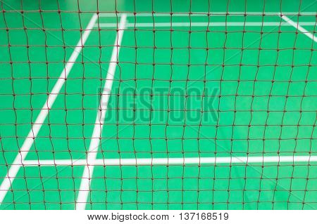 Red badminton net in a green court with white line.