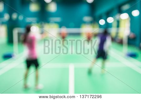 Blurred people playing badminton in green court.