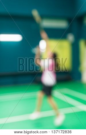 Blurred woman playing badminton in green court.