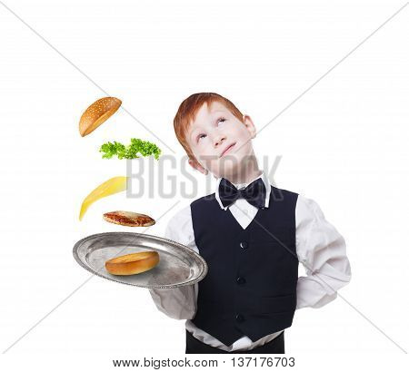 Little waiter dreaming with tray, serving hamburger. Cheeseburger levitates with separated toppings. Flying burger layers. Smiling redhead child boy in suit isolated at white background