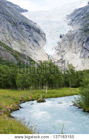 Briksdalsbreen glacier at summer with mountain river from melted ice on foreground. Jostedalsbreen National Park in Norway.