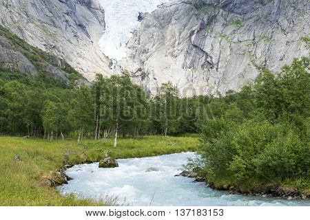 Briksdalsbreen glacier at summer with mountain river from melted ice on foreground. Jostedalsbreen National Park in Norway.