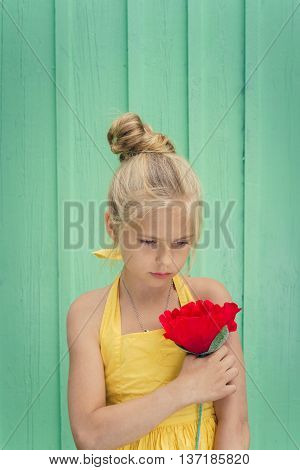 Sad young blond girl holding a red flower. Space for text