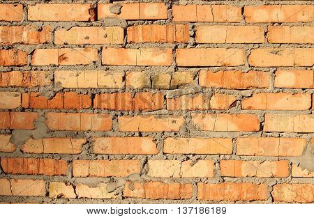 New brick wall, terracotta color with the remains of cement and coarse stitching, illuminated by bright sunshine.