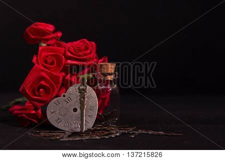 Red ribbon roses, timeless heart clock, minute hand and clearly glass bottle in the dark