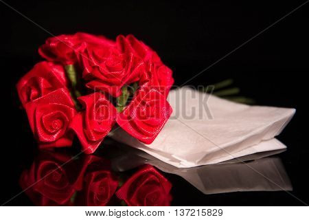 Red ribbon roses and white paper reflect in dark and blur